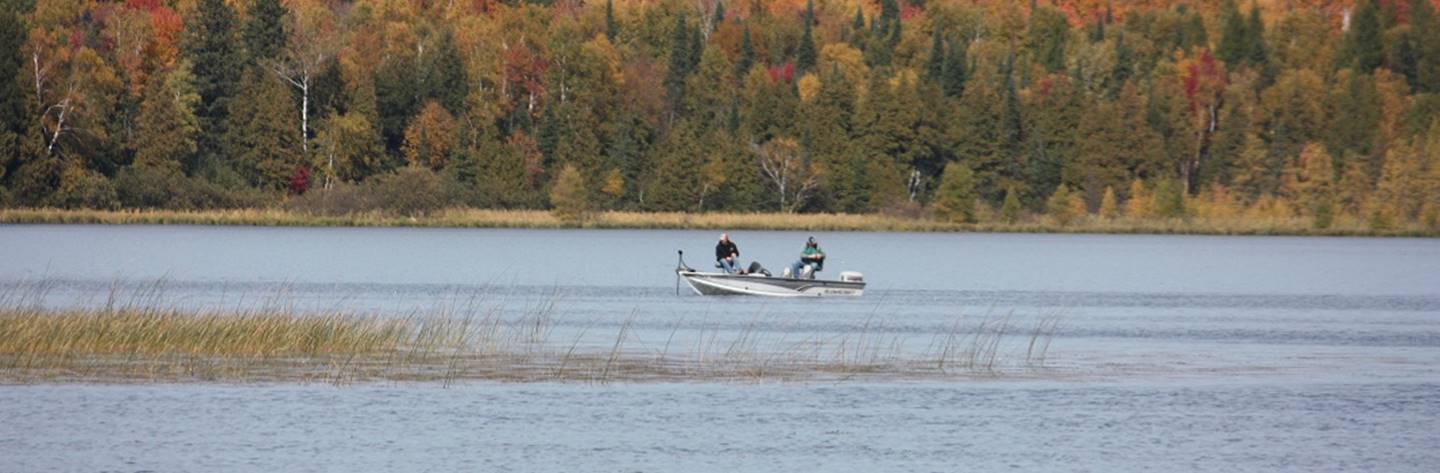 Fishermen troll Langlade County Lake in the fall as the beautiful leaves along the banks change color.
