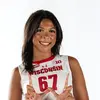 A person in a Wisconsin volleyball uniform, jersey number 67, poses making a “W” with her hands. The background is plain white.