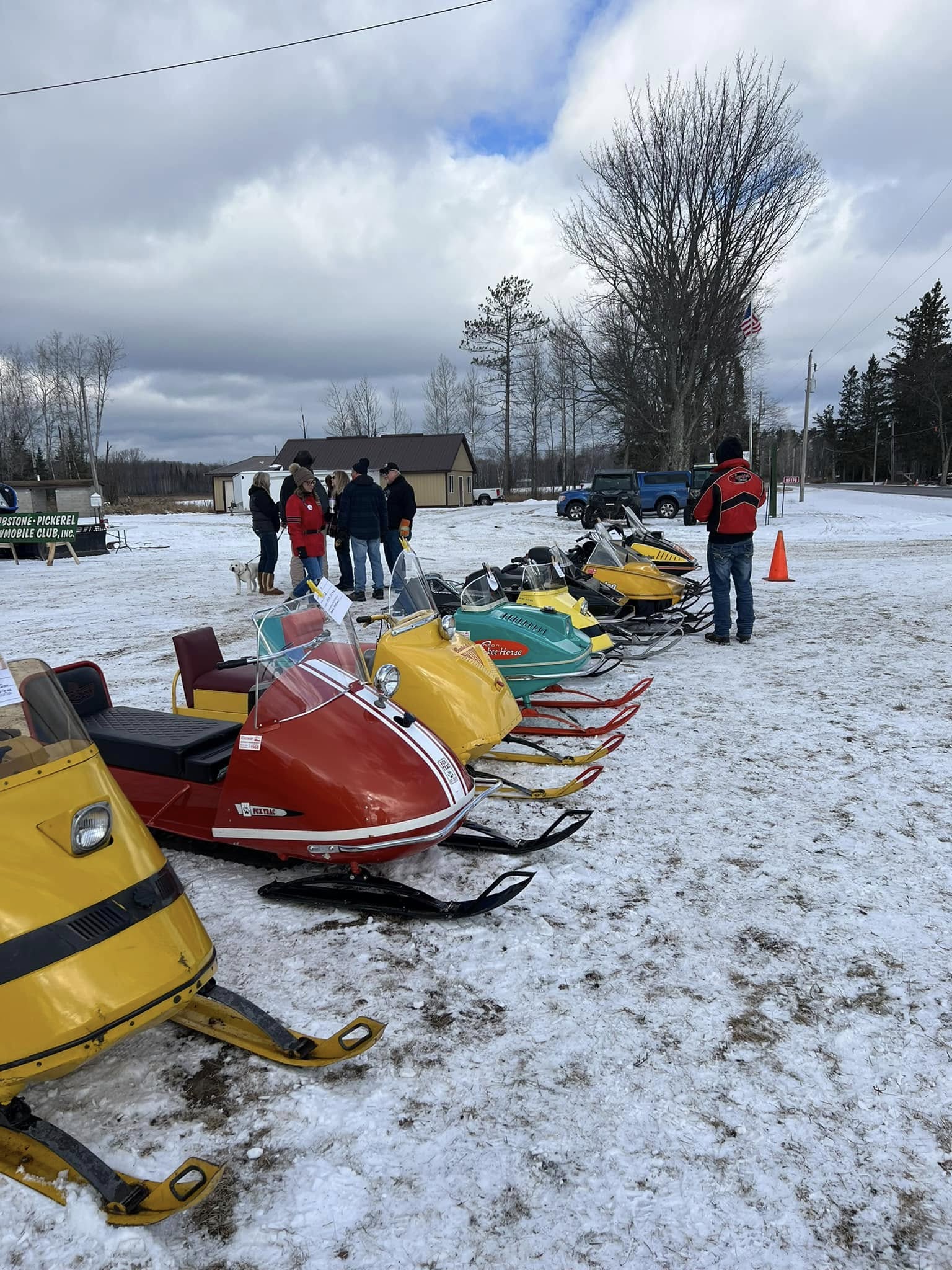 A colorful lineup of vintage snowmobiles is proudly displayed on the snow-covered grounds.