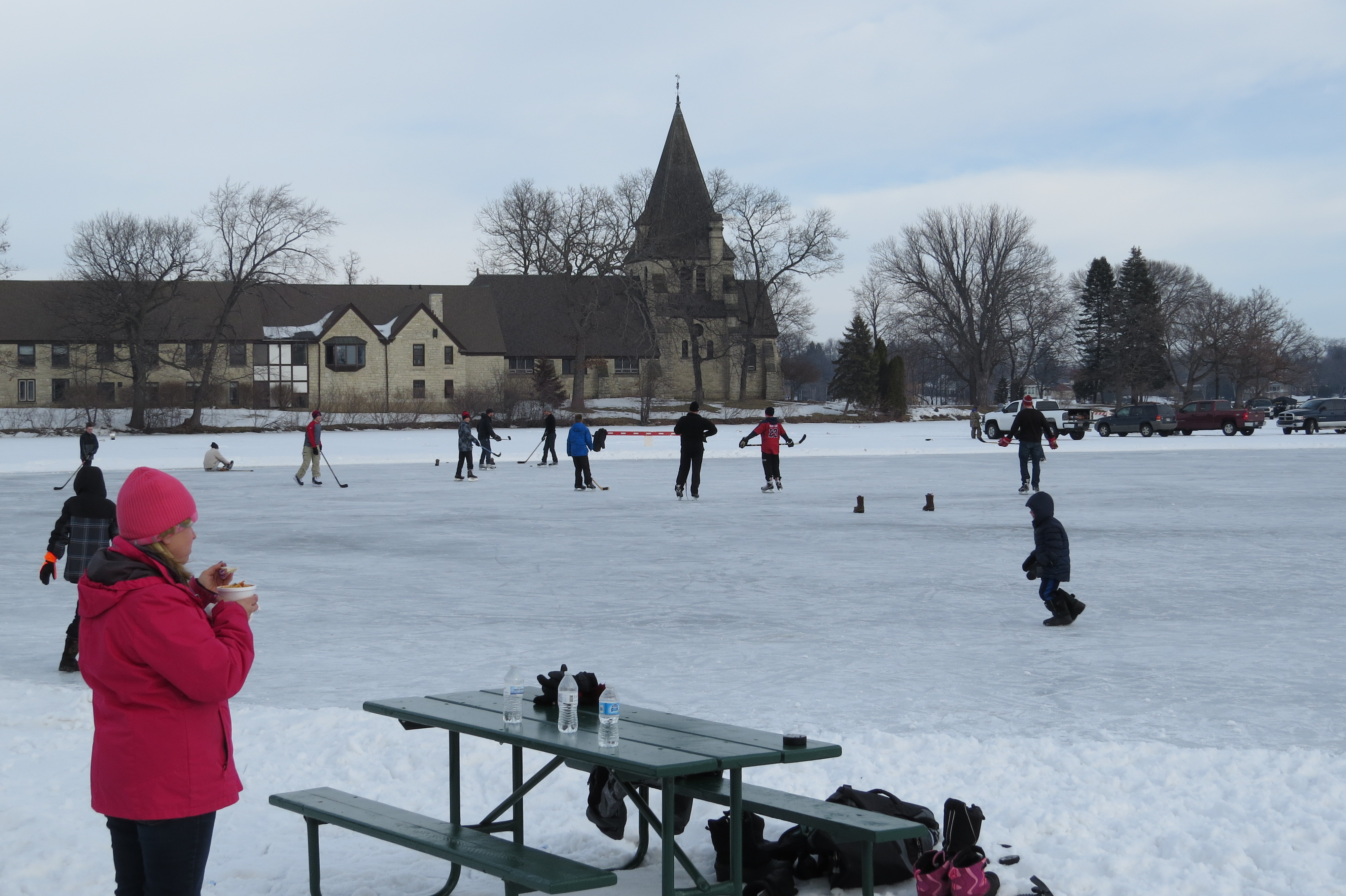 A Chili Fest attendee enjoys a warm bowl of chili while she enjoys watching ice skating and hockey on the lake.