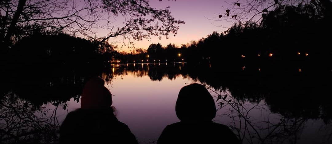 two people looking over Lake Joanis and seeing the tiki torch lit path from afar.