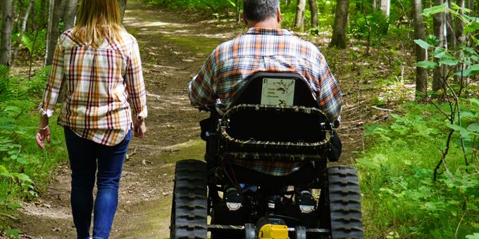 An individual using the tracked outdoor wheelchair next to an individual walking a hiking trail at Thunder Mountain Overlook