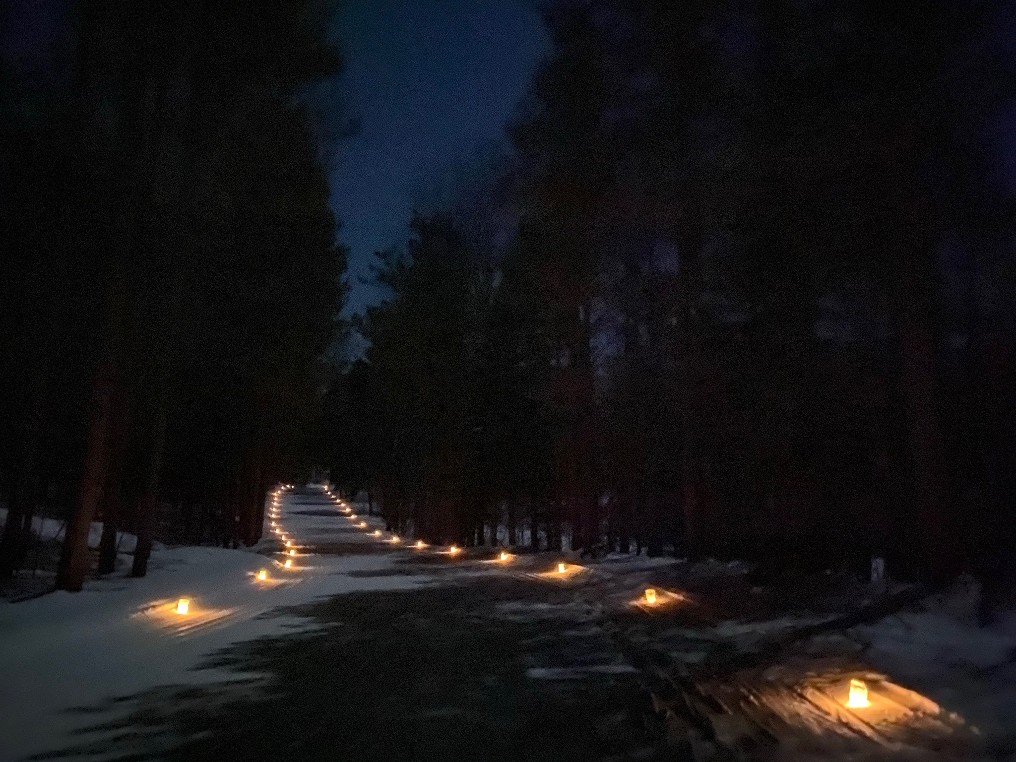 A candlelit ski trail is lit by a full moon.