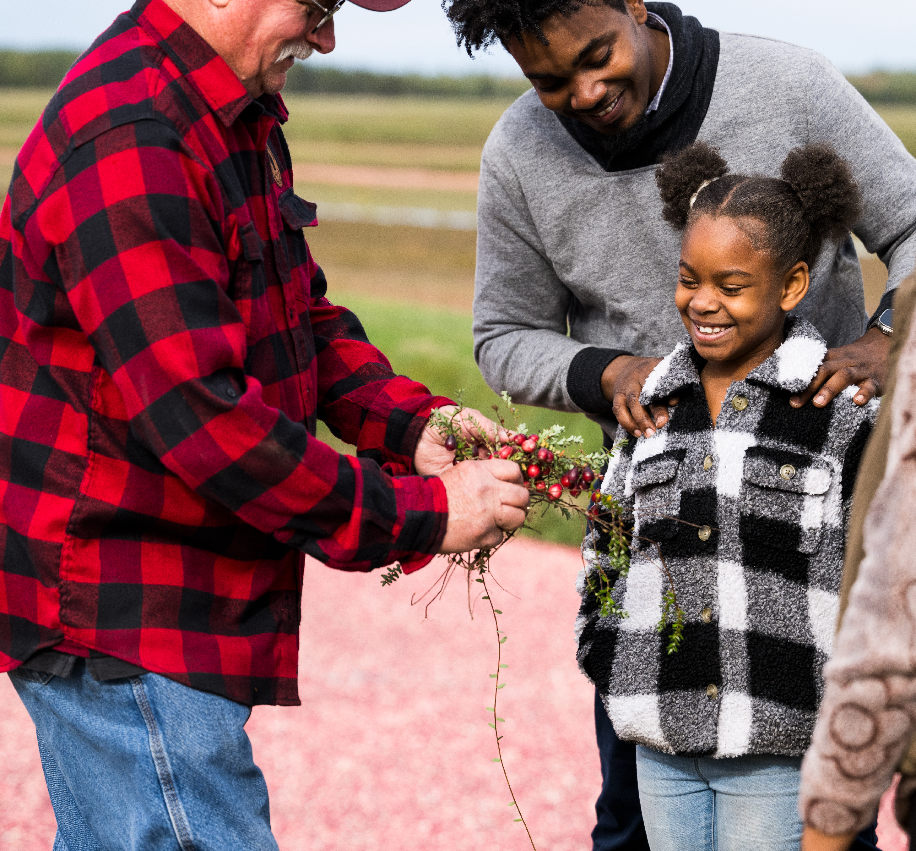 little girl smiling and looking at some cranberries being shown to her by a cranberry farmer