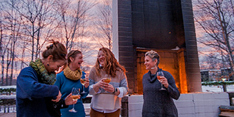Friends have drinks outside near a firepit with a giant chimney