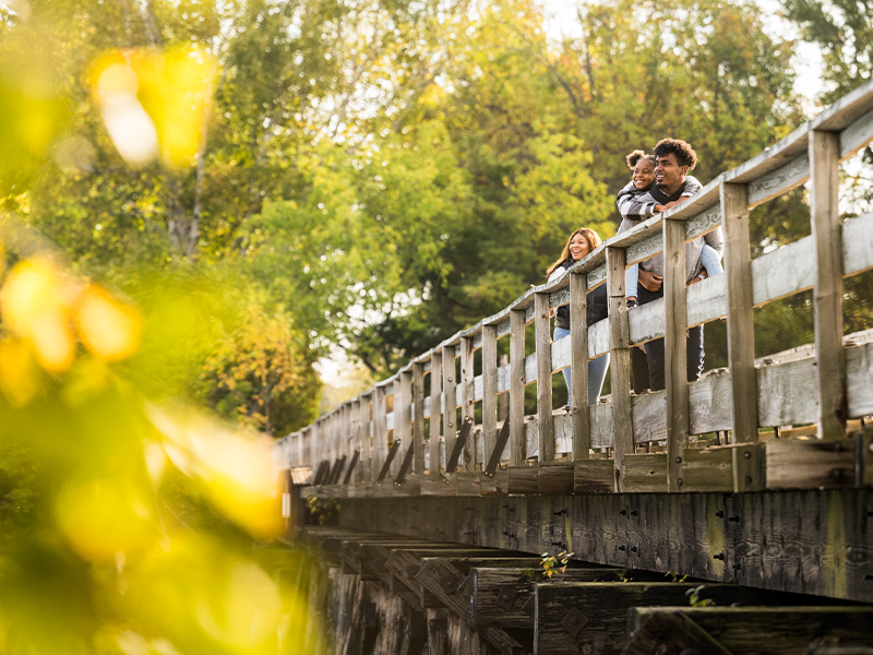 family walking along a bridge while dad carries little girl on his back