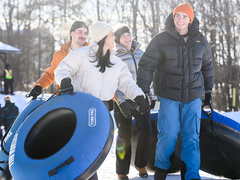 Friends in snow suits carrying snow tubes