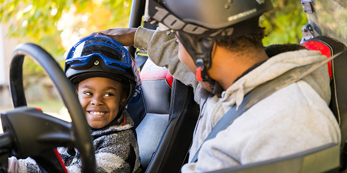 little boy smiling at his dad while sitting in an ATV