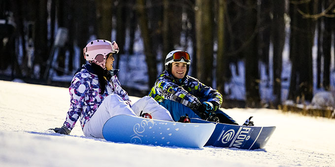 Friends on snowboards, sitting and taking a break on the snow-covered hill