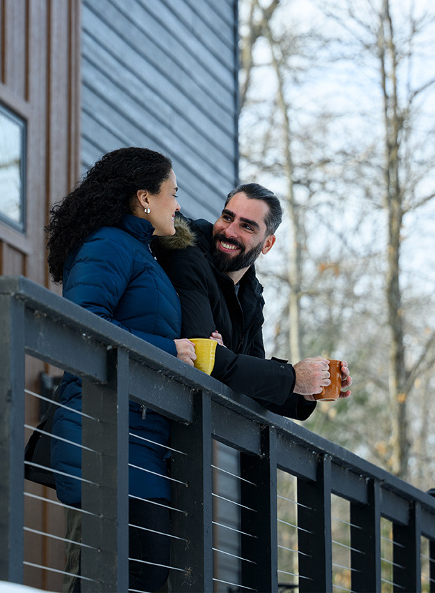 Couple drinking coffee on a balcony outside of a house in the woods