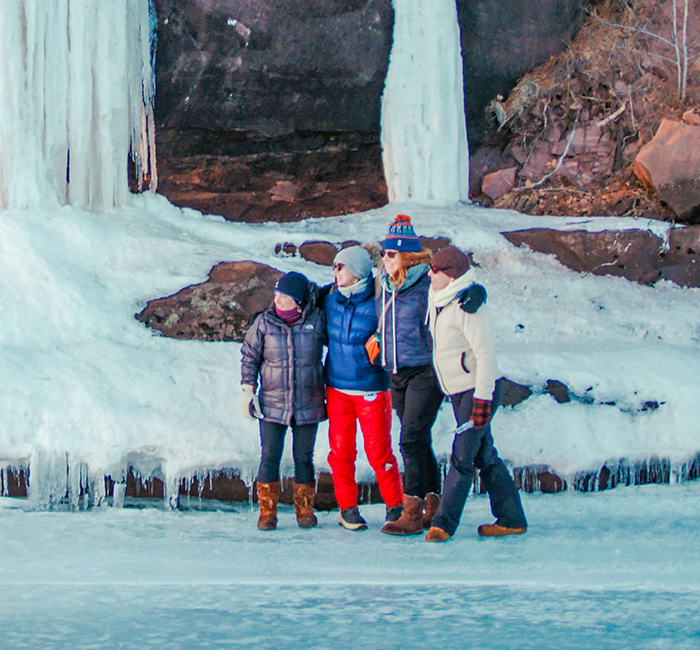 Friends huddled together in front of cliffs covered in snow and icicles