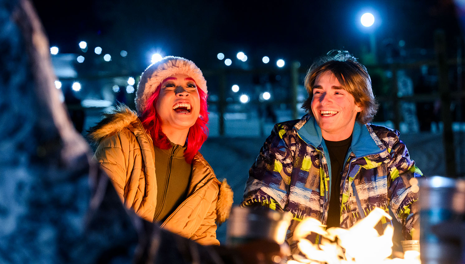 Friends laughing around a fire, outside at night