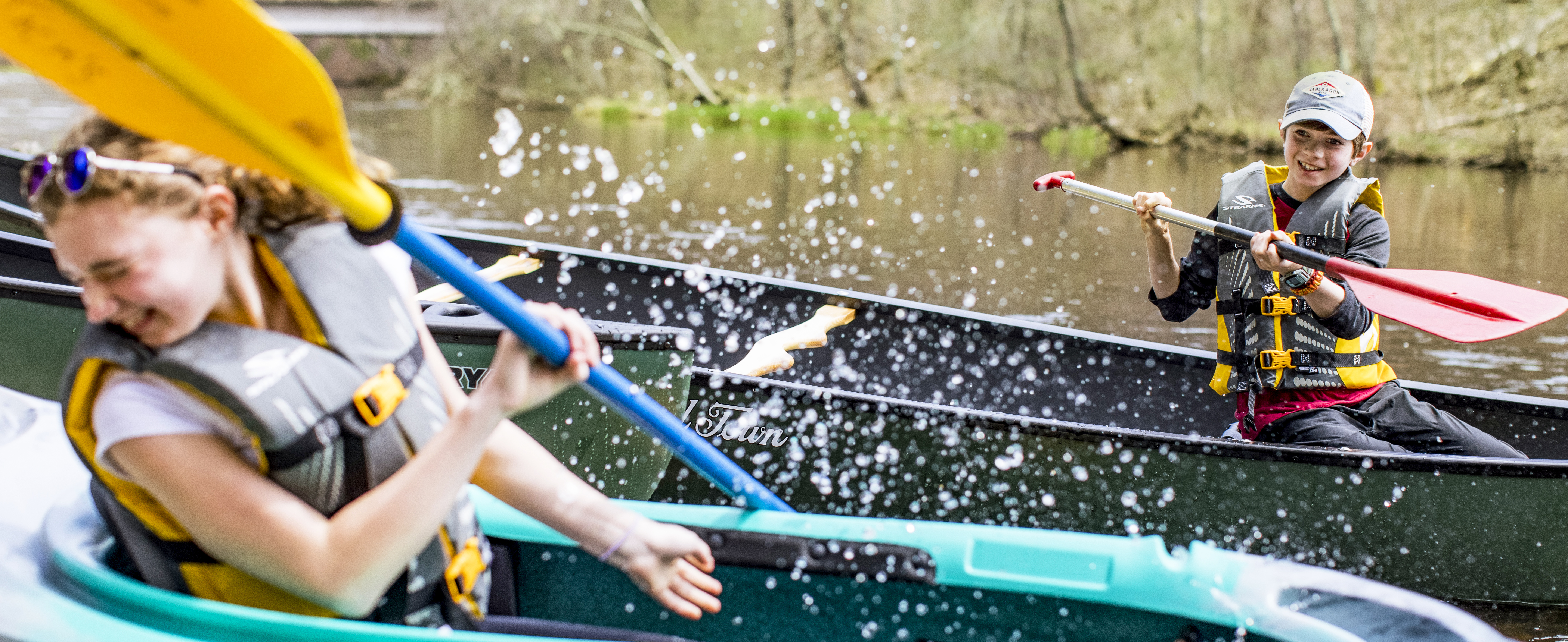Brother and Sister splashing each other with water using their kayak paddles