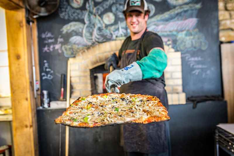 man holds out pizza at pizza farm