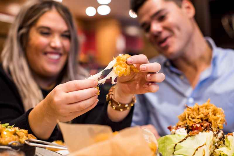 a man and a woman out of focus stretching the cheese on a cheese curd