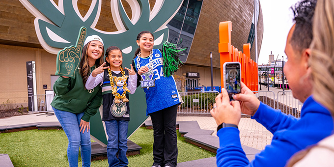 family takes a photo in front of the milwaukee bucks logo at the deer district