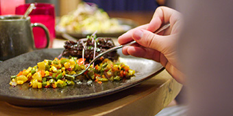 A close up of a person taking a scoop of food off of a dark plate