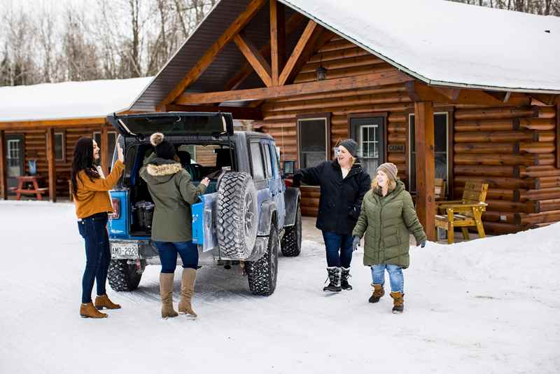 Group of friends unloading their car in front of a log cabin