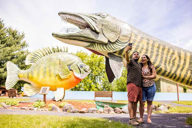 couple taking a selfie in front of the large musky at the fresh water fishing hall of fame