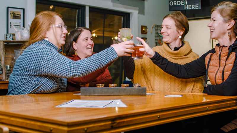 friends-cheers-beer-flight-bayfield Friends cheers a beer flight at a wooden table in a restaurant