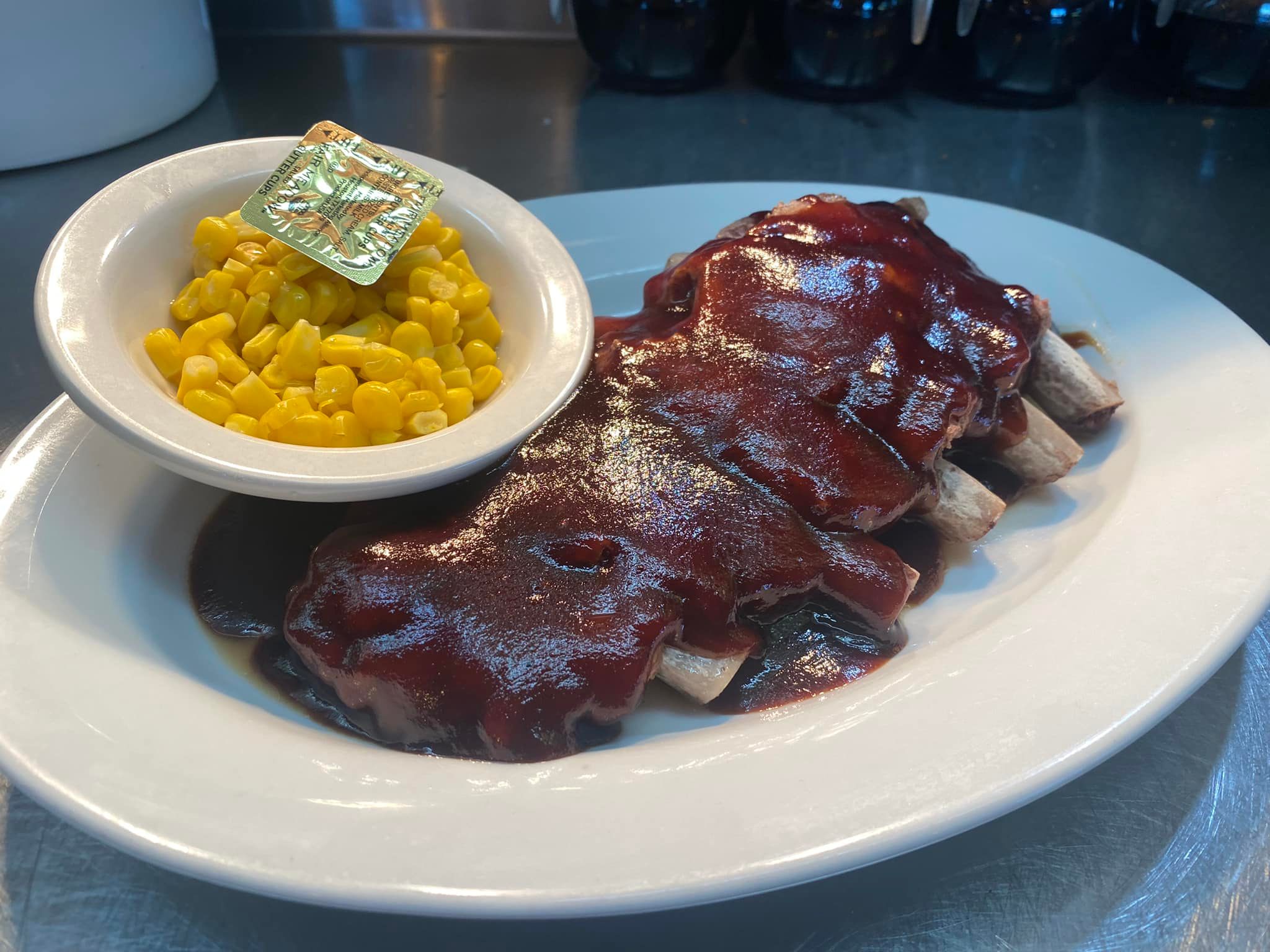 A generous portion of saucy BBQ ribs served with a side of sweet corn—Truck’s Place brings the flavor with comfort food favorites that satisfy every appetite.
