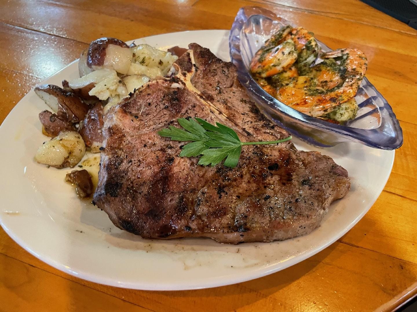 A grilled T-bone steak is served with seasoned roasted potatoes and a side of garlic herb shrimp—one of many hearty, flavorful dishes served at Foxwood Tavern.
