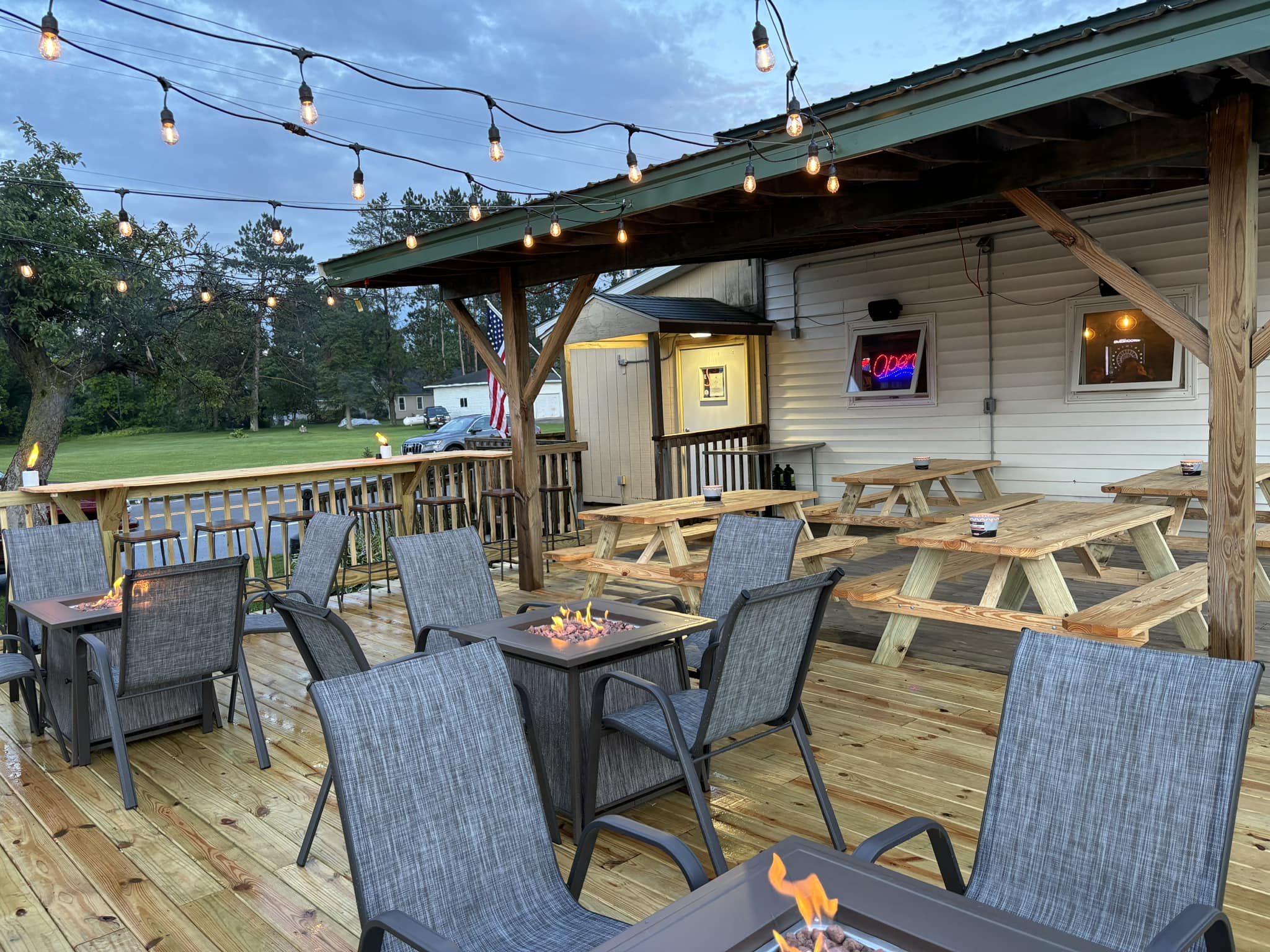 Foxwood Tavern’s outdoor patio glows under string lights at dusk, featuring cozy fire tables, picnic seating, and a relaxed atmosphere perfect for summer evenings in Langlade County.