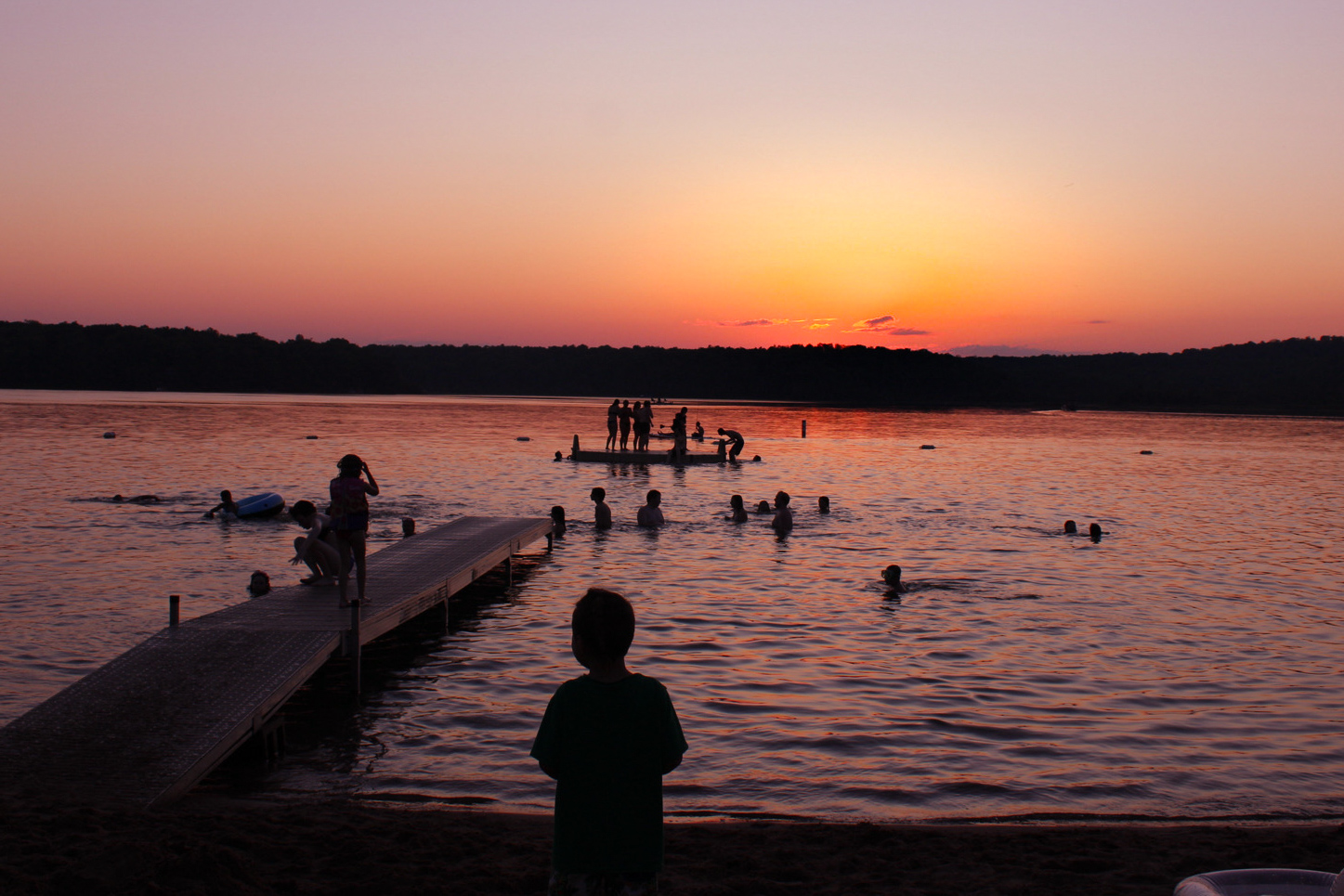 As the sun sets over White Lake, people unwind on the sandy beach and splash near the swimming dock and raft.