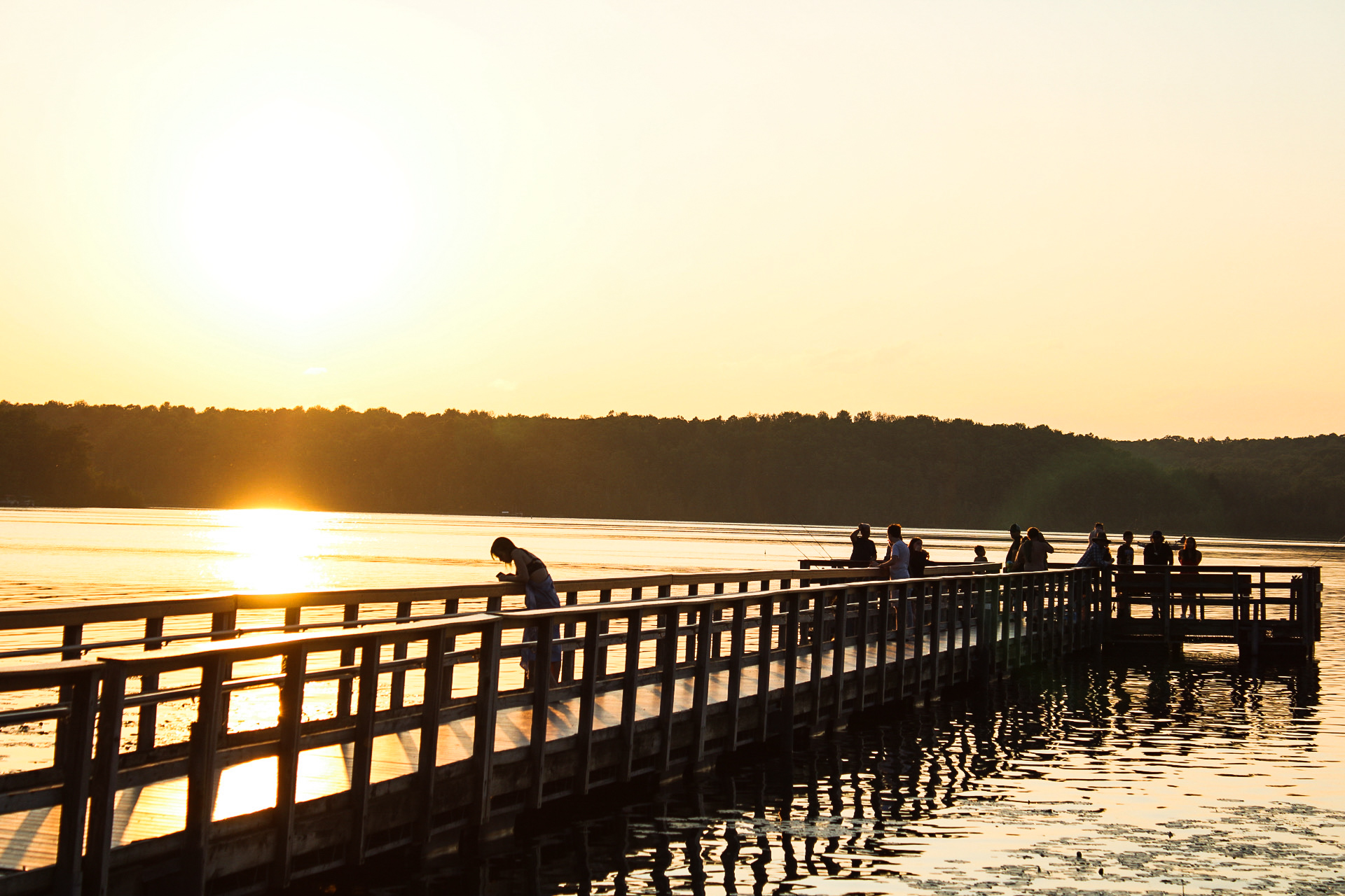 People gather on White Lake’s fishing pier, casting lines and sharing laughs as the sun sets over the tranquil waters.