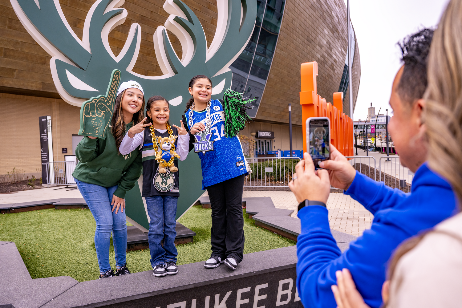 Father Takes Photo Of Daughters With Merch In Front Of Large Bucks Logo In Deer District, Milwaukee