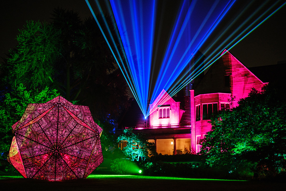 The historic Paine mansion at night awash in colorful lights, with a sculpture large enough to walk in.