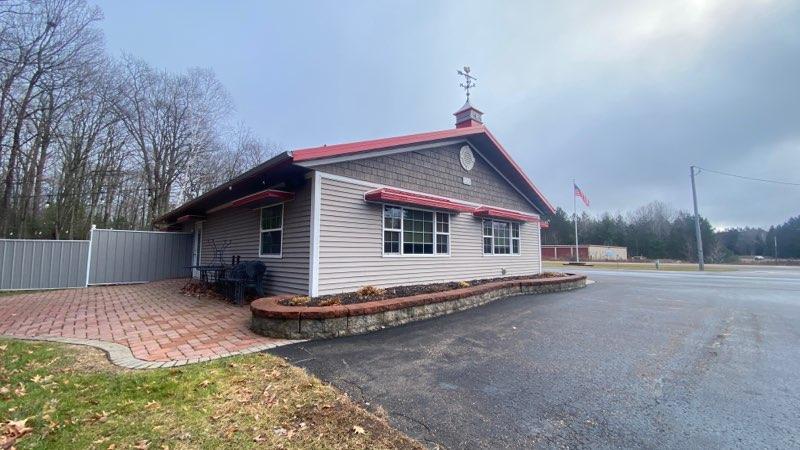 A different angle of the café building, showing a red-trimmed roof, outdoor seating on a brick patio, and a quiet parking area bordered by trees and open sky.
