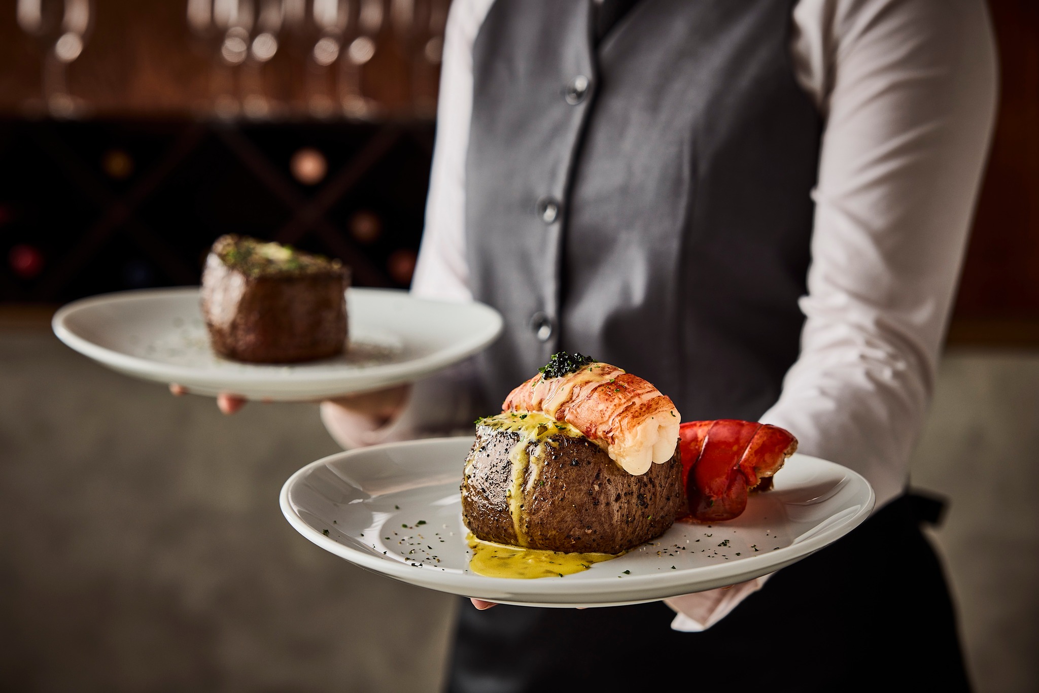 Waiter presents two dishes: one with a steak, the other with a steak topped with lobster.