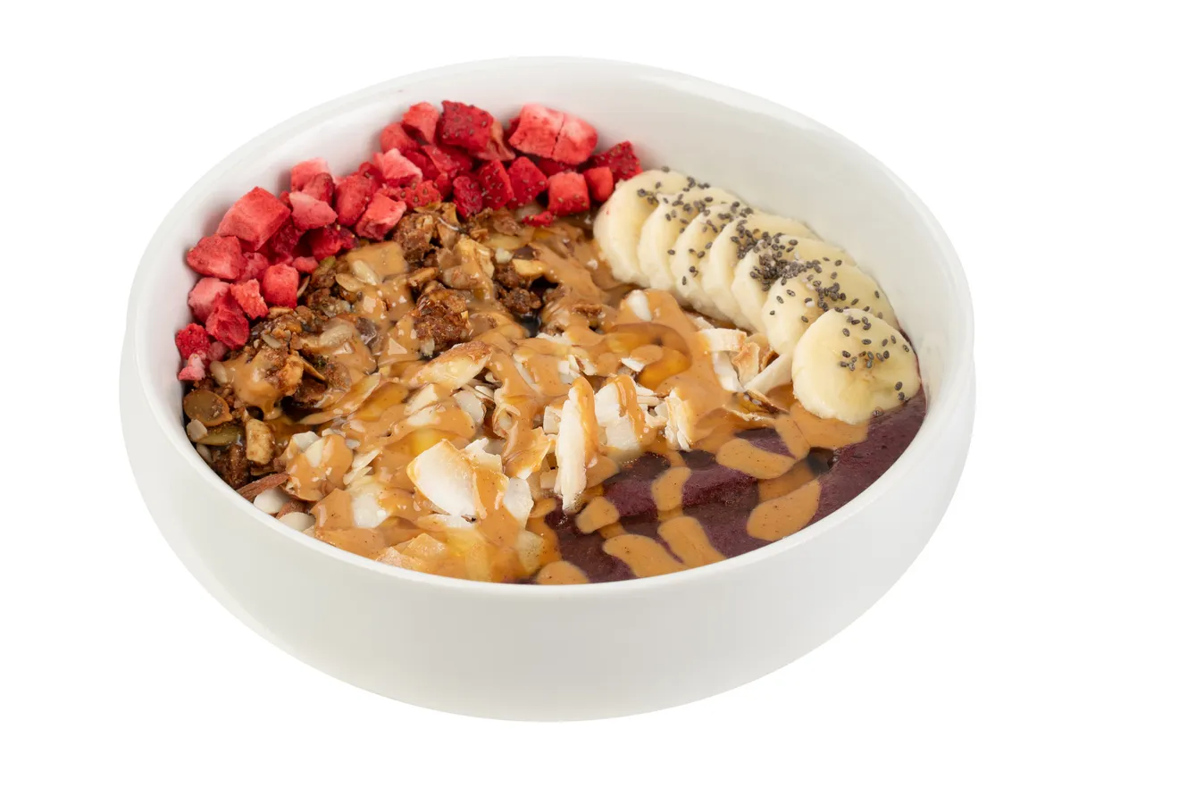 A white bowl filled with smoothie base is topped with a colorful variety of fruits, seeds, and other healthy toppings.