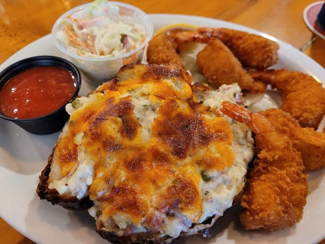 A cheesy twice-baked potato is loaded with flavor and served alongside golden fried shrimp and creamy coleslaw—bringing bold taste to the table at Foxwood Tavern.