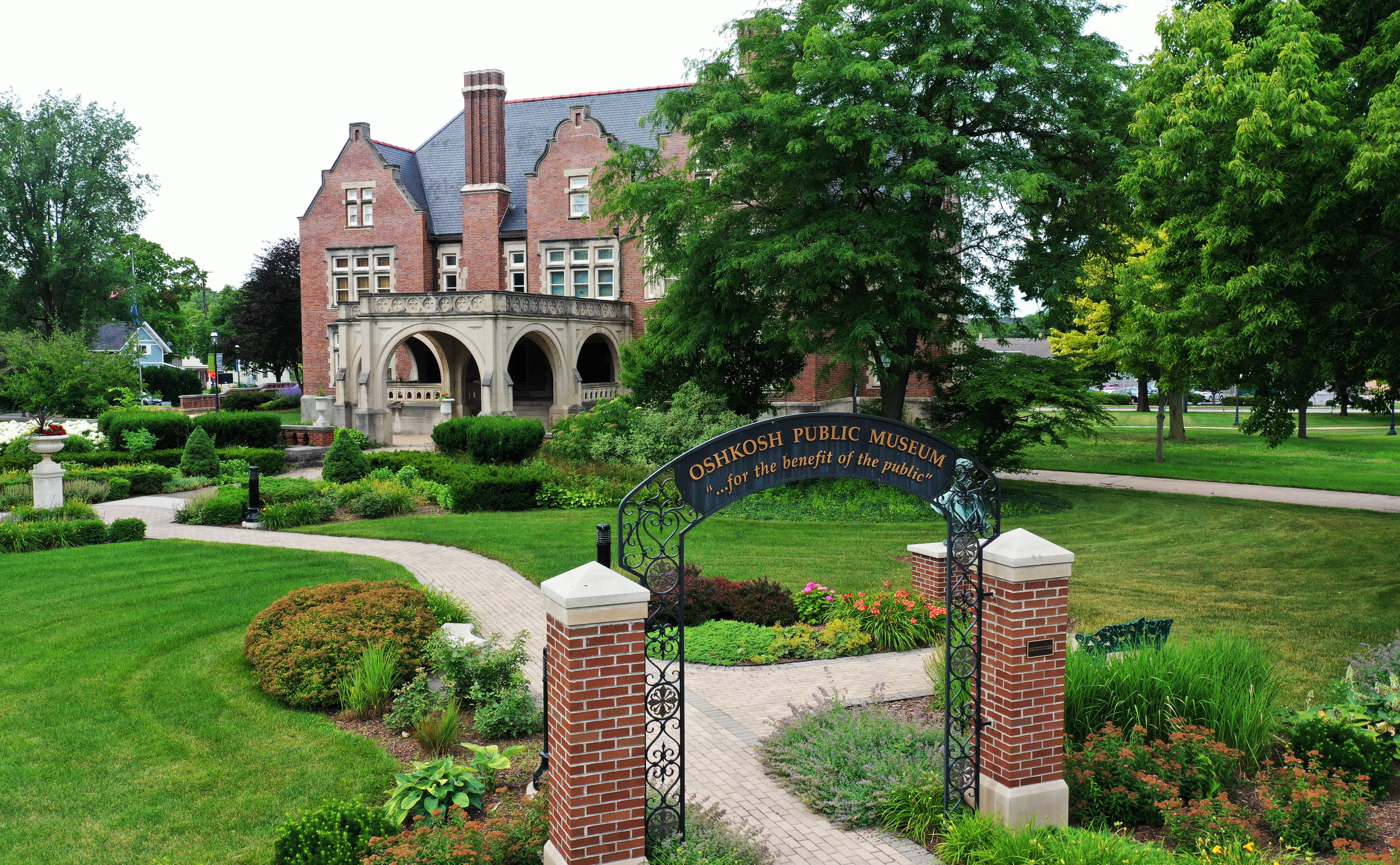 View of the front lawns of the Historic Sawyer Home, including an archway reading "Oshkosh Public Museum" and "for the benefit of the public," a reference to Edgar Sawyer's bequest of the home to the City of Oshkosh.