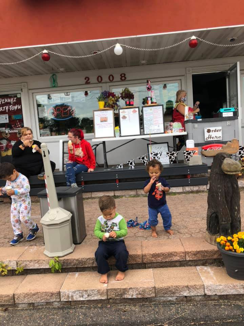 Families and children gather outside an old-fashioned ice cream shop, enjoying sweet treats on a cozy patio. With colorful cones in hand, the kids sit and smile, capturing a joyful summer moment.