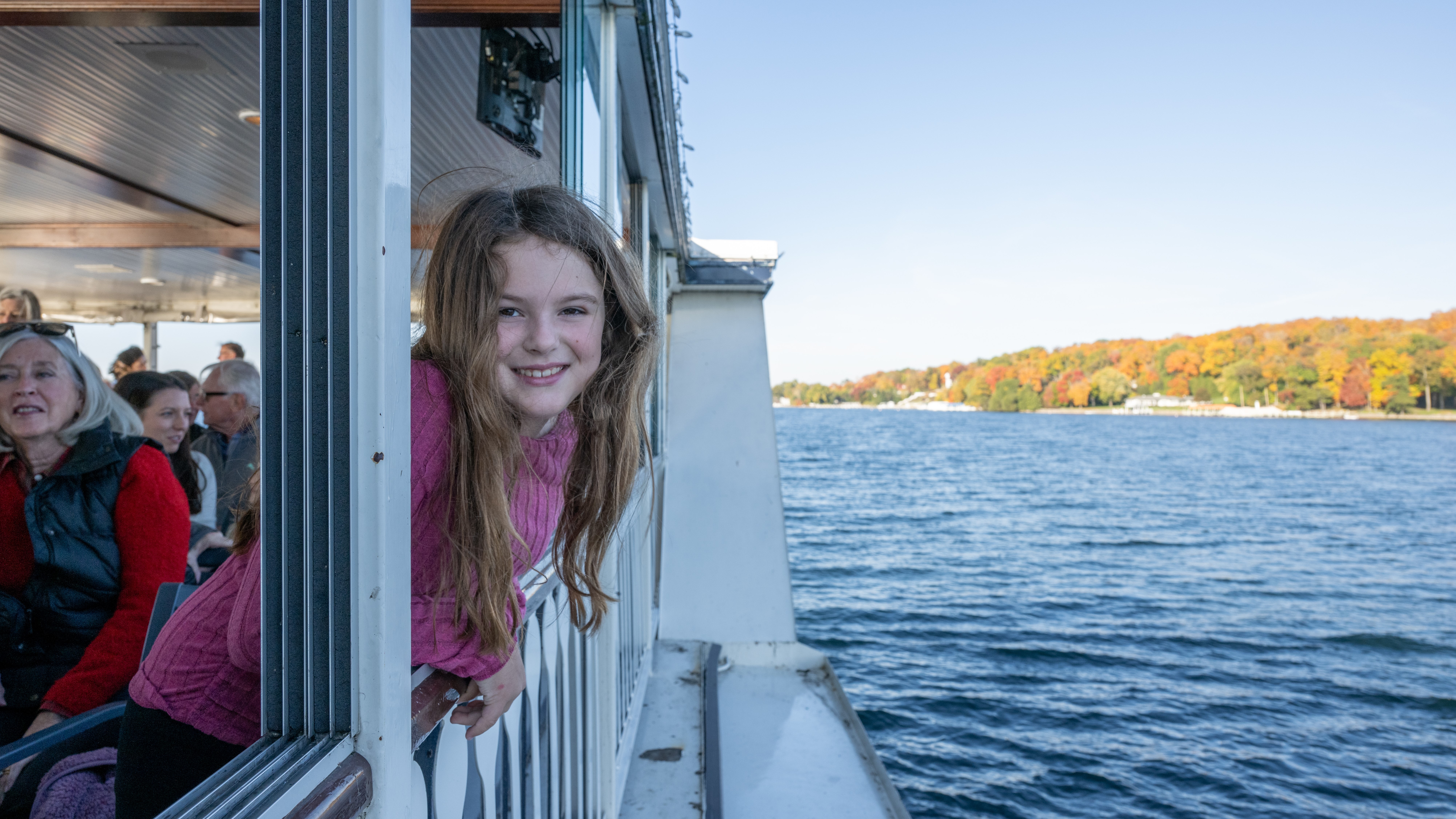 A young girl sticking her head out of the window of a large boat on the lake during fall
