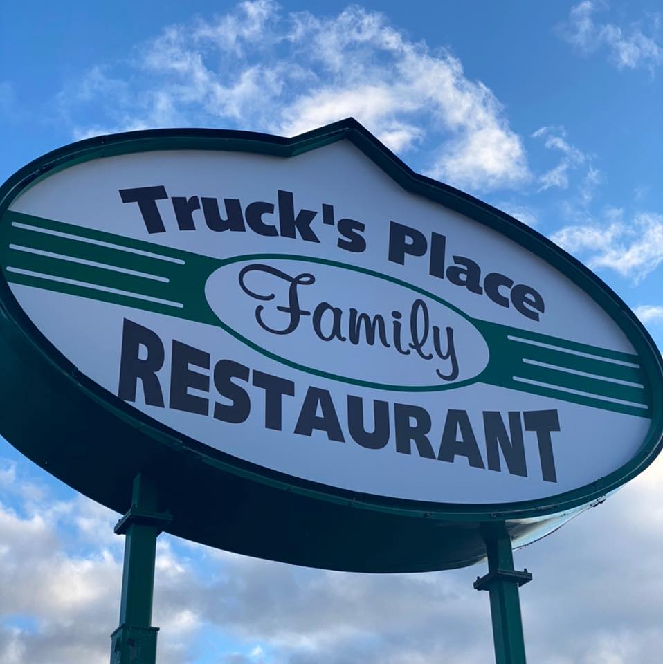 The Truck’s Place Family Restaurant sign stands tall against a blue sky with scattered clouds, inviting guests to enjoy classic comfort food and hometown hospitality in Langlade County.
