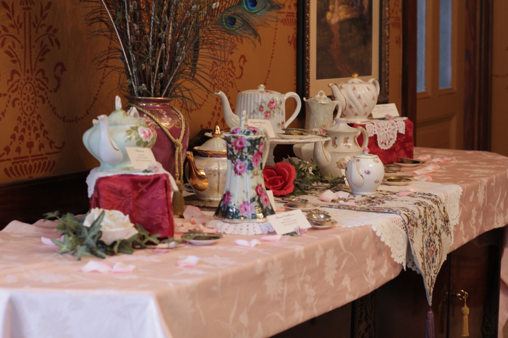 A decorated table set with floral arrangements, vintage teapots, and delicate porcelain pottery displayed for an elegant event or showcase.