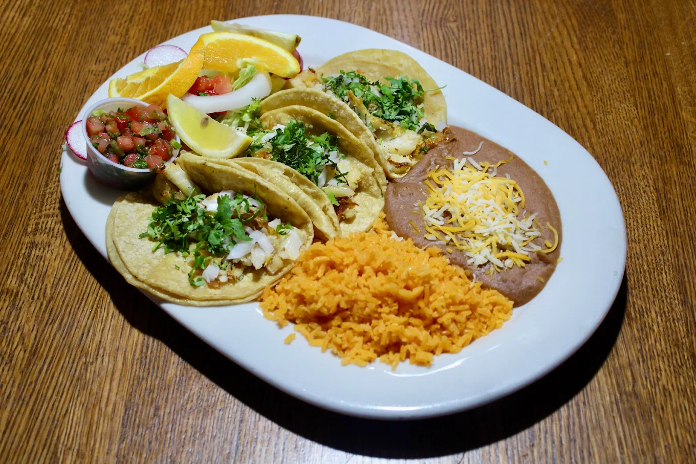Plate with three tacos served alongside rice and refried beans, garnished with salsa.