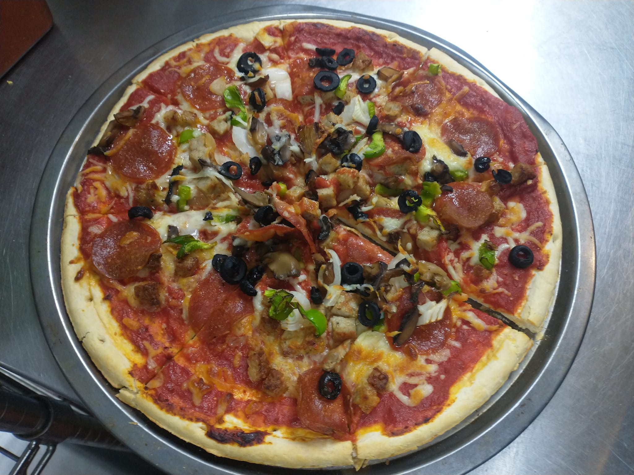 A fresh-baked supreme pizza on a metal tray, topped with pepperoni, sausage, olives, onions, mushrooms, and green peppers, with melted cheese and a golden crust.