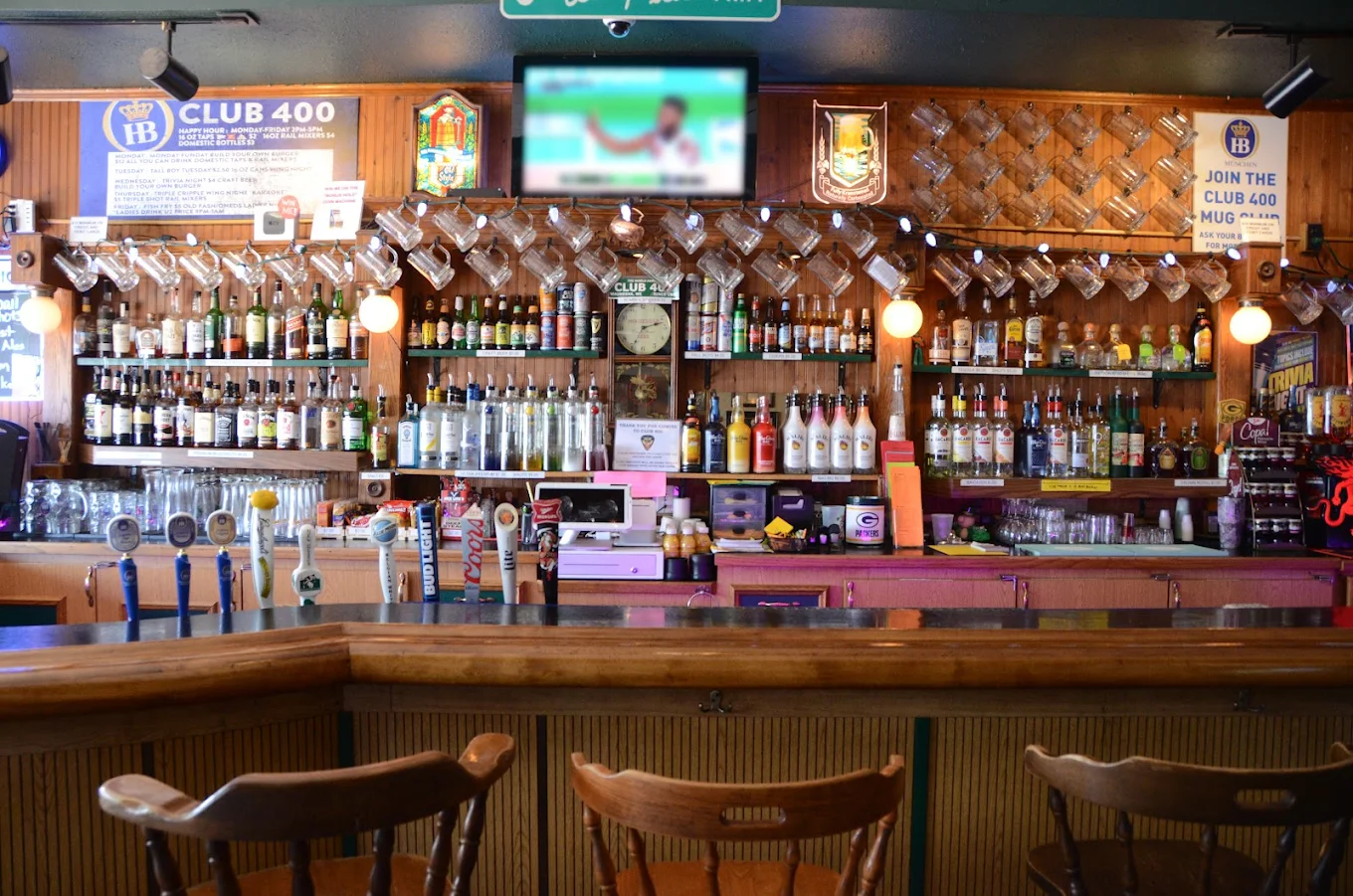 Interior view of a bar with bottles, beer taps, and wooden furnishings.